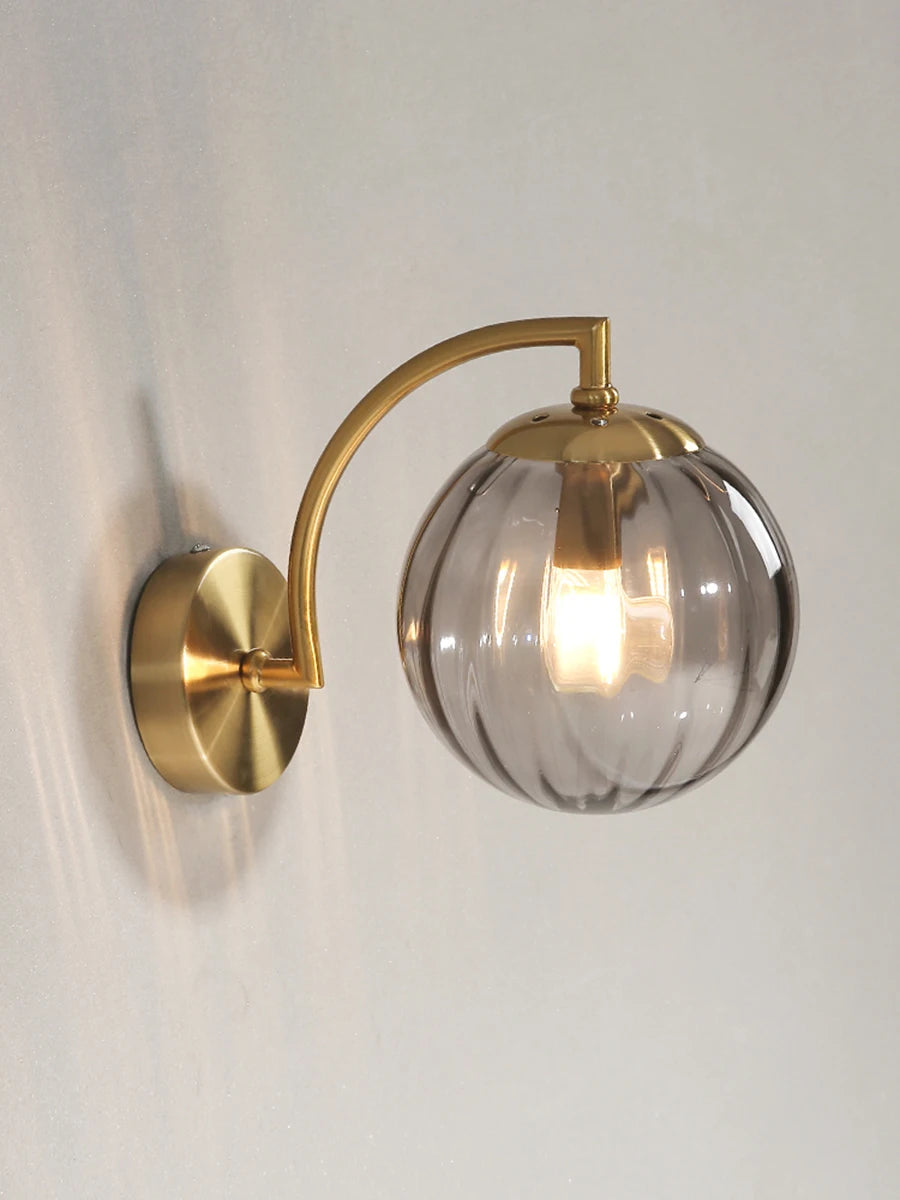 Modern Nordic glass LED wall sconce mounted beside a bed in a contemporary bedroom with warm ambient lighting.