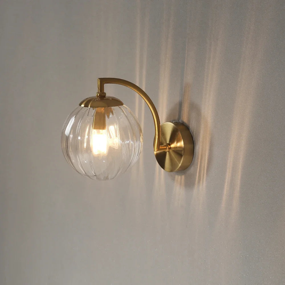 Modern Nordic glass LED wall sconce mounted beside a bed in a contemporary bedroom with warm ambient lighting.
