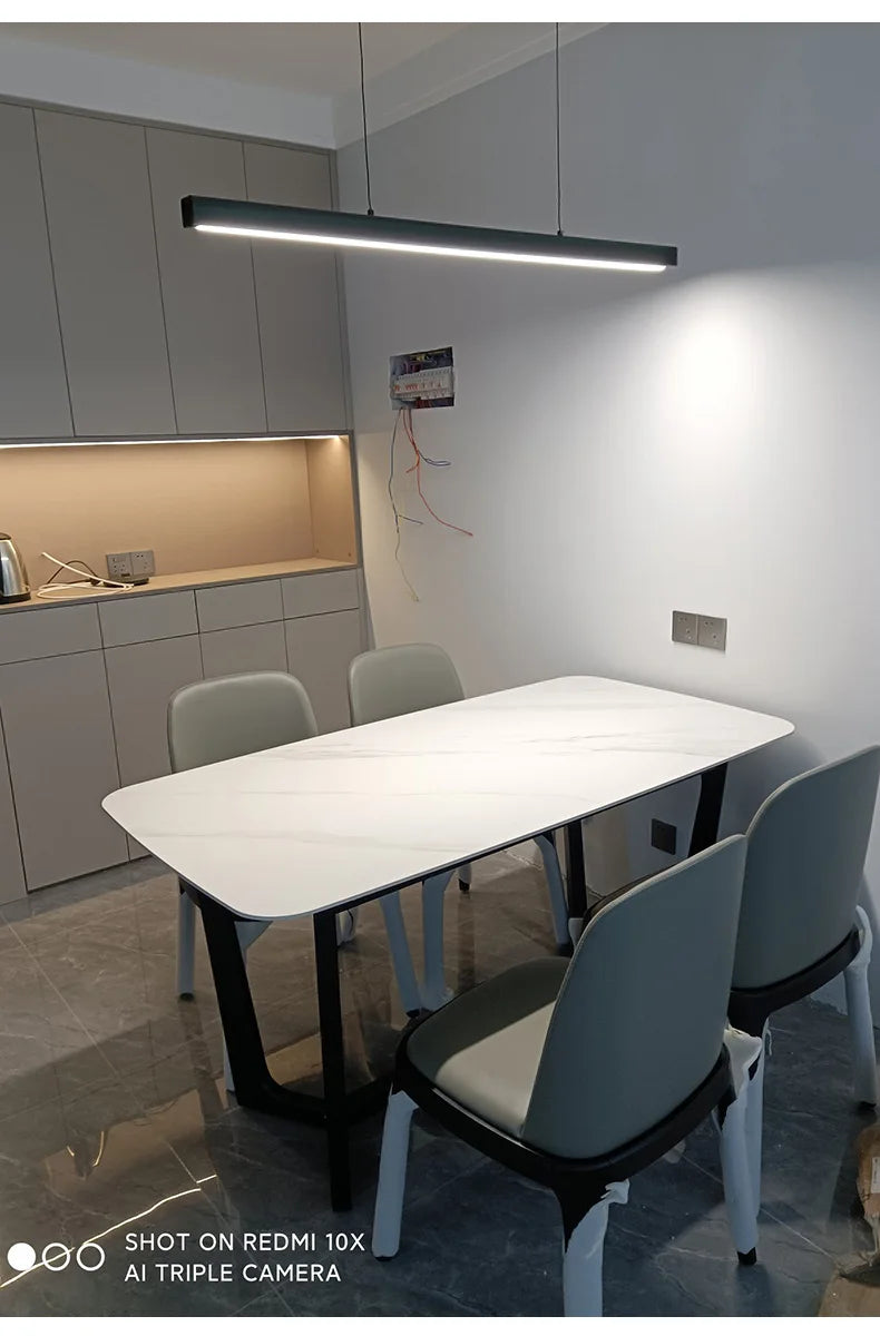 Modern linear LED pendant light suspended above a dining table in a contemporary dining room.