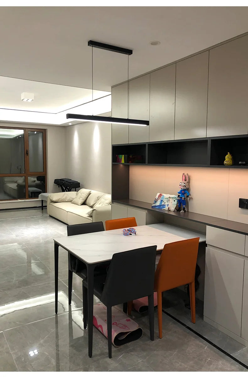 Modern linear LED pendant light suspended above a dining table in a contemporary dining room.