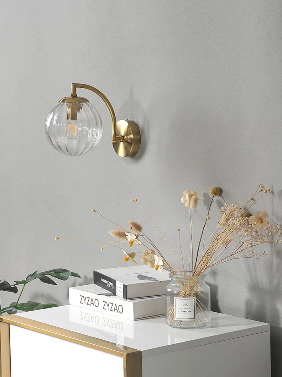 Modern Nordic glass LED wall sconce mounted beside a bed in a contemporary bedroom with warm ambient lighting.