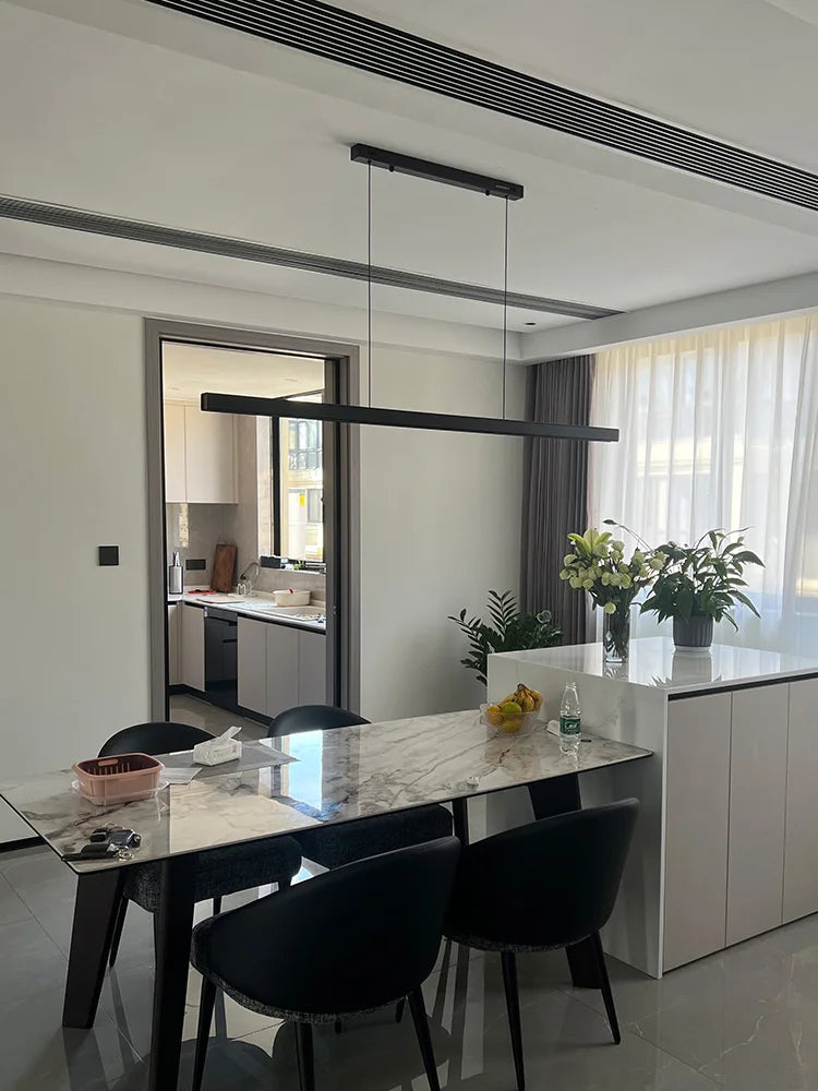 Modern linear LED pendant light suspended above a dining table in a contemporary dining room.