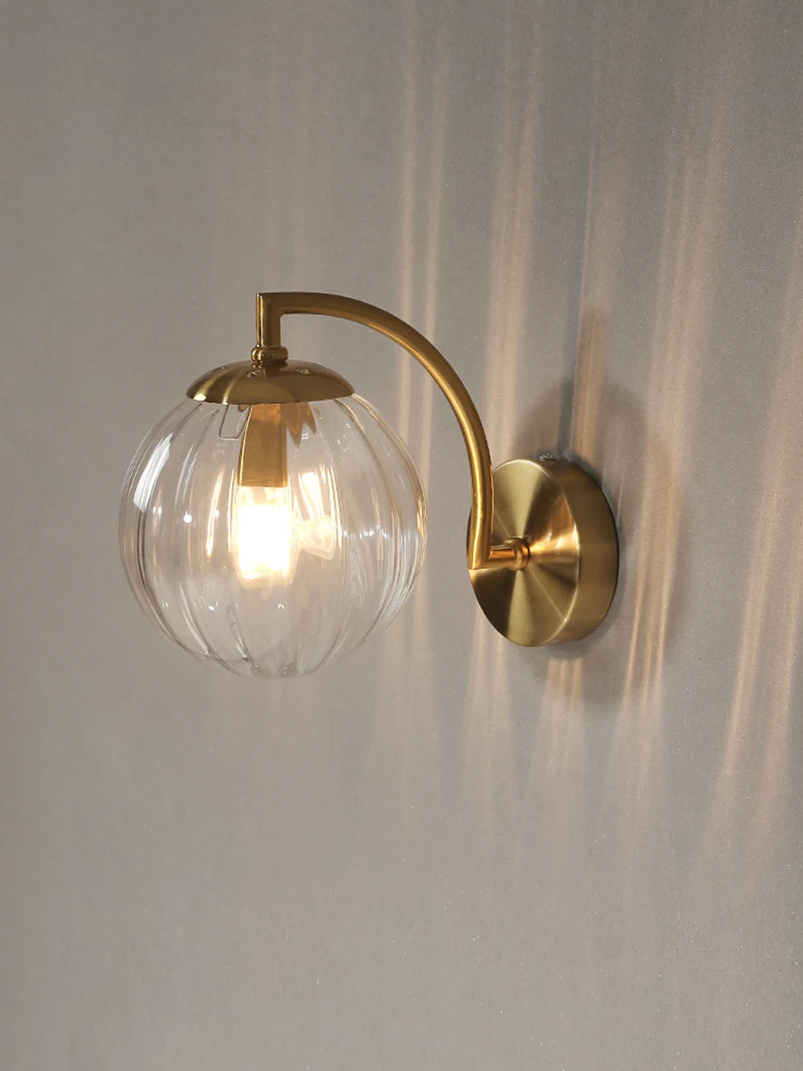 Modern Nordic glass LED wall sconce mounted beside a bed in a contemporary bedroom with warm ambient lighting.