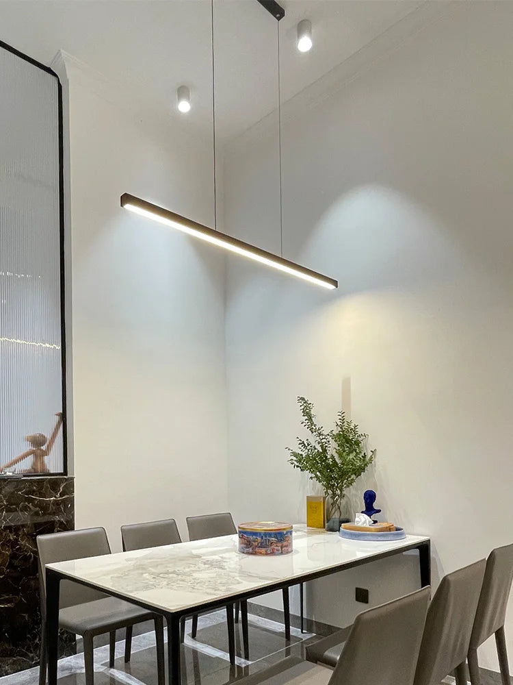 Modern linear LED pendant light suspended above a dining table in a contemporary dining room.