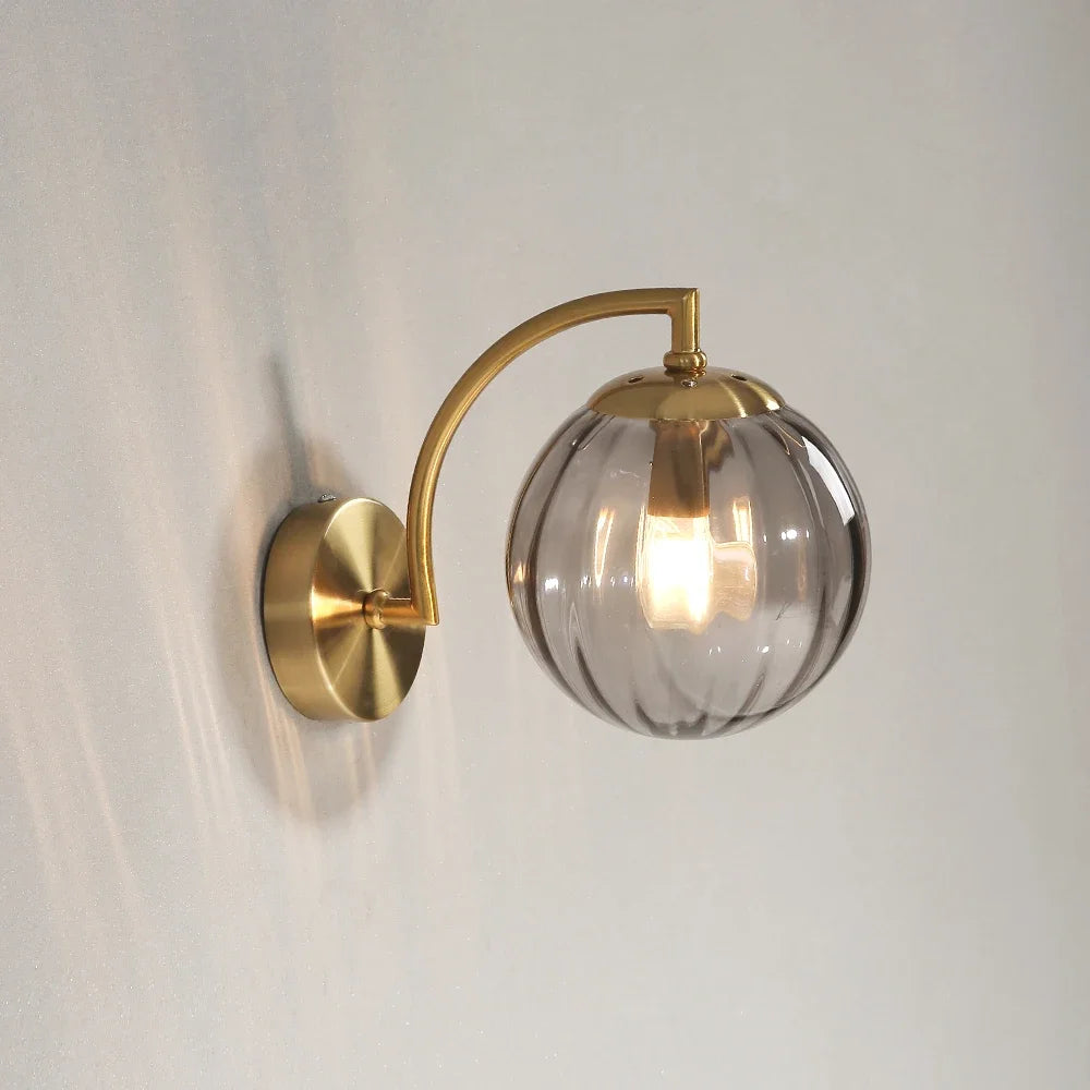 Modern Nordic glass LED wall sconce mounted beside a bed in a contemporary bedroom with warm ambient lighting.
