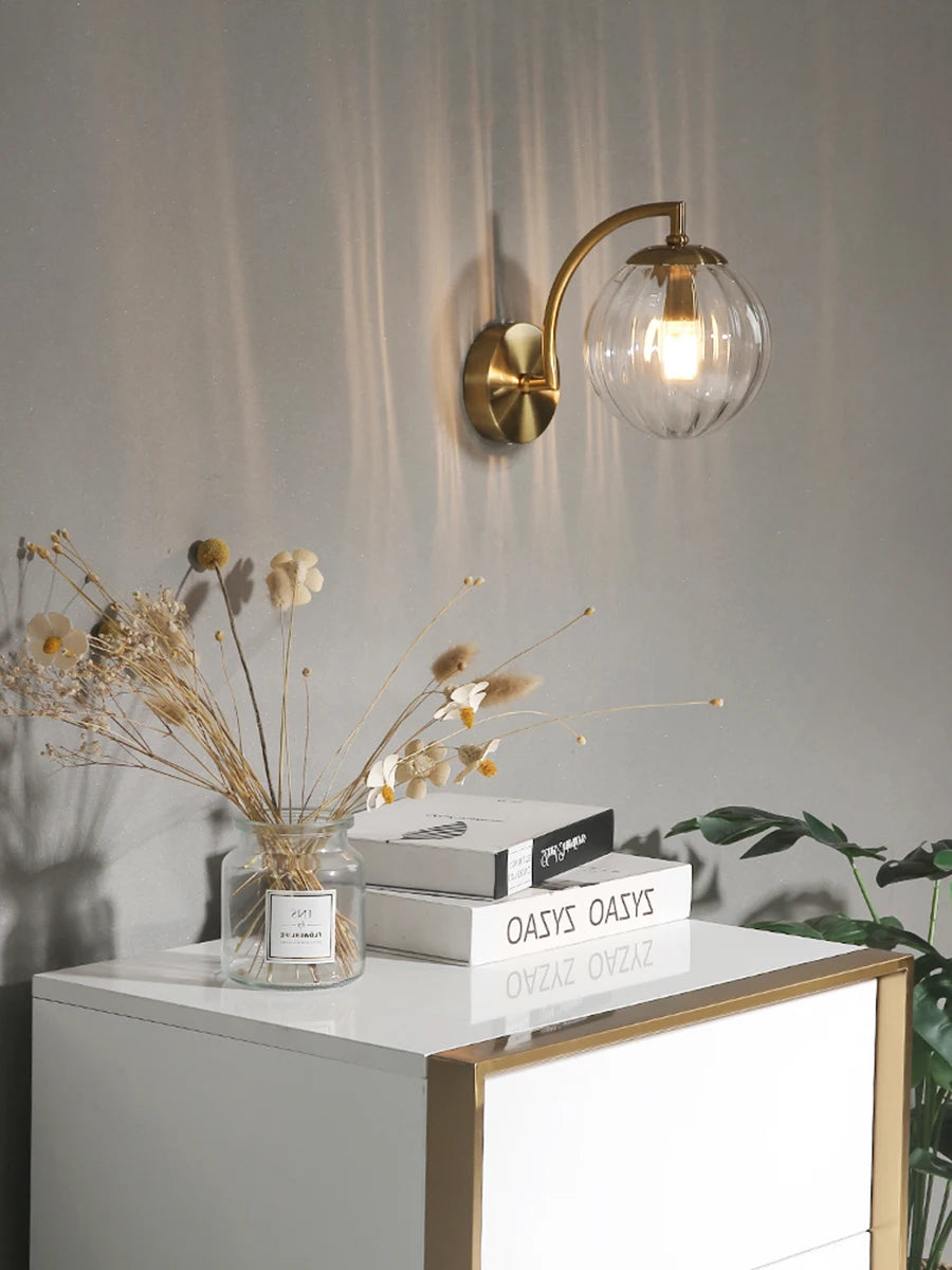 Modern Nordic glass LED wall sconce mounted beside a bed in a contemporary bedroom with warm ambient lighting.
