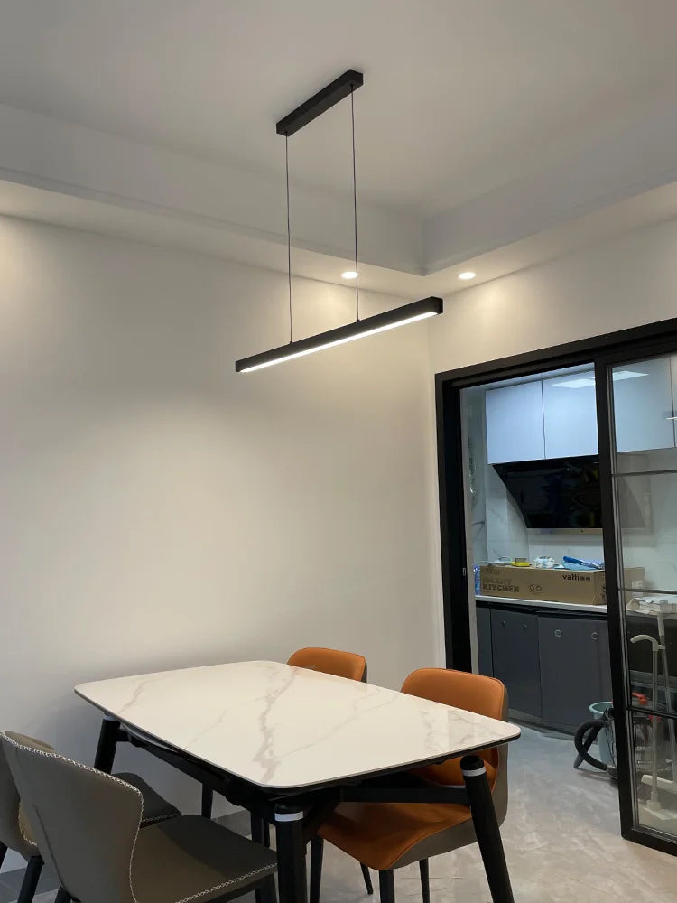 Modern linear LED pendant light suspended above a dining table in a contemporary dining room.