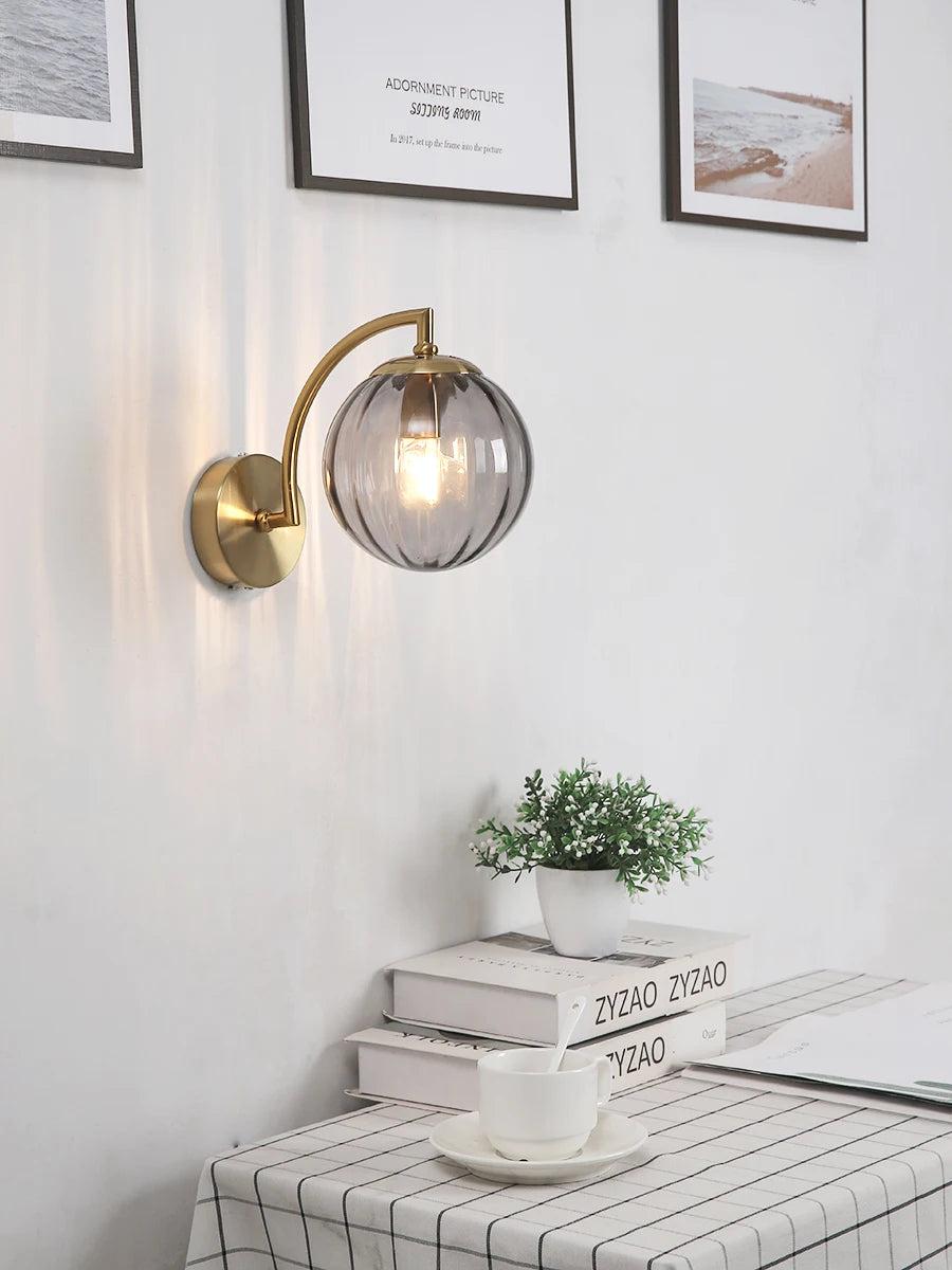 Modern Nordic glass LED wall sconce mounted beside a bed in a contemporary bedroom with warm ambient lighting.