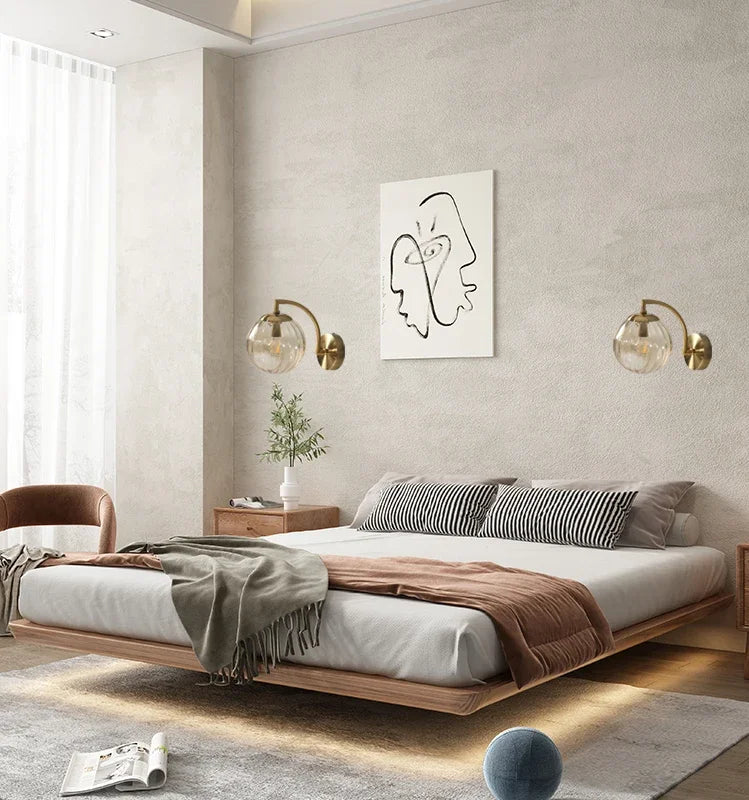Modern Nordic glass LED wall sconce mounted beside a bed in a contemporary bedroom with warm ambient lighting.