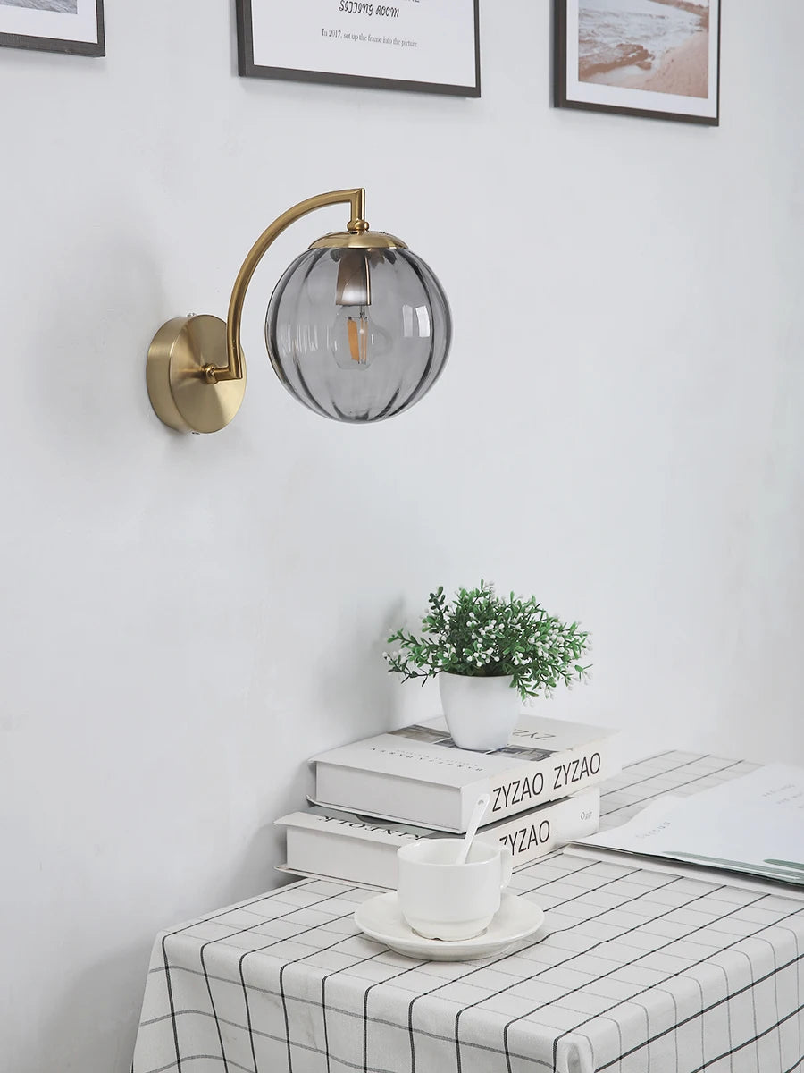 Modern Nordic glass LED wall sconce mounted beside a bed in a contemporary bedroom with warm ambient lighting.